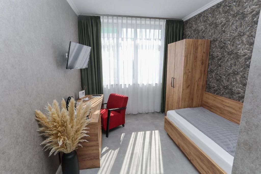 Ein kleines Zimmer mit einem Bett, einem Schreibtisch, einem Sessel, einem Fernseher und einem Kleiderschrank.