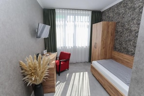 A compact room with a bed, a desk, a chair, a TV, and a wardrobe.
