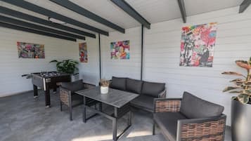 Un área de estar al aire libre moderna con mesa de fútbol, un sofá y una mesa con planta en maceta.
