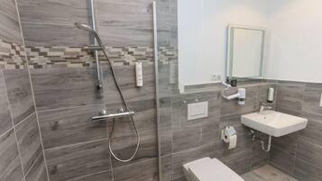 Ein modernes Badezimmer mit einer gläsernen Dusche, einem weißen Waschbecken und einer Toilette.
