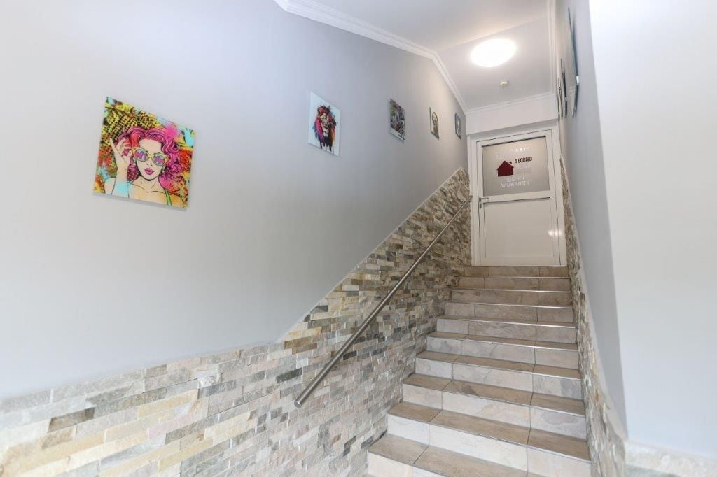 Eine Treppe mit Steinmauer und Handlauf, die zu einer Tür mit Haussymbol und Schrift führt.