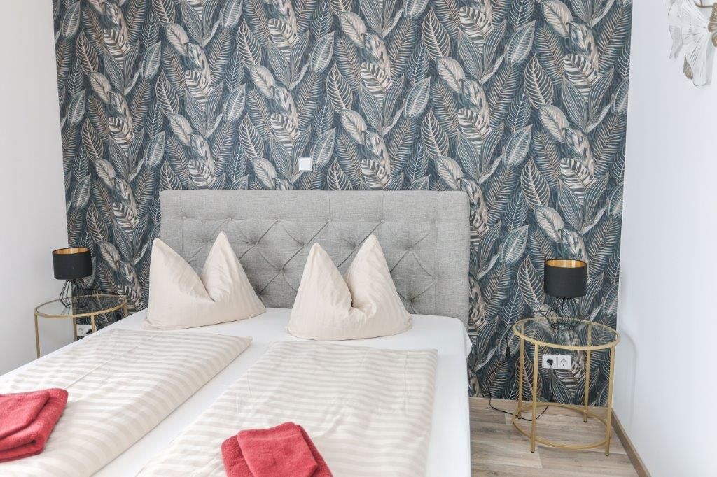 Un dormitorio con cama, almohadas, cabecera y dos mesitas de noche con lámparas.
