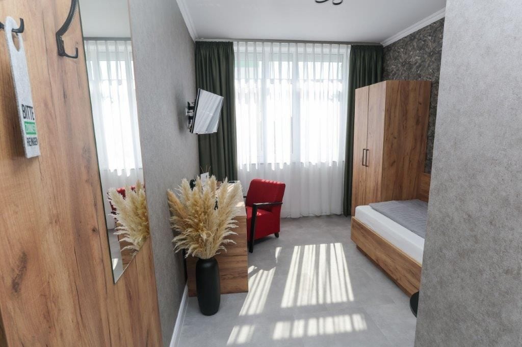 Una habitación moderna con una cama, una silla roja, un armario de madera y un televisor instalado en la pared.