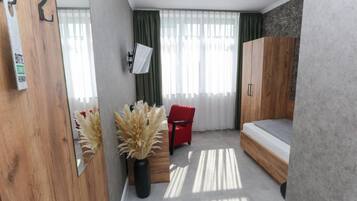 Una habitación moderna con una cama, una silla roja, un armario de madera y un televisor instalado en la pared.