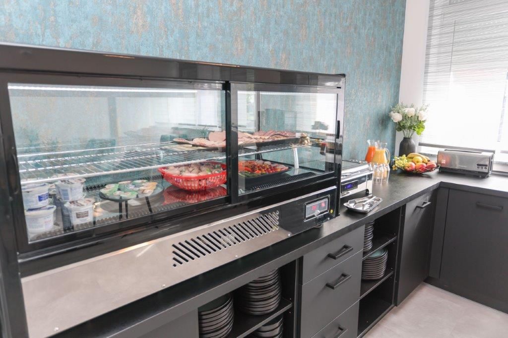 Een buffetgedeelte met een glazen vitrine, een schaal fruit en een broodrooster op het aanrecht.