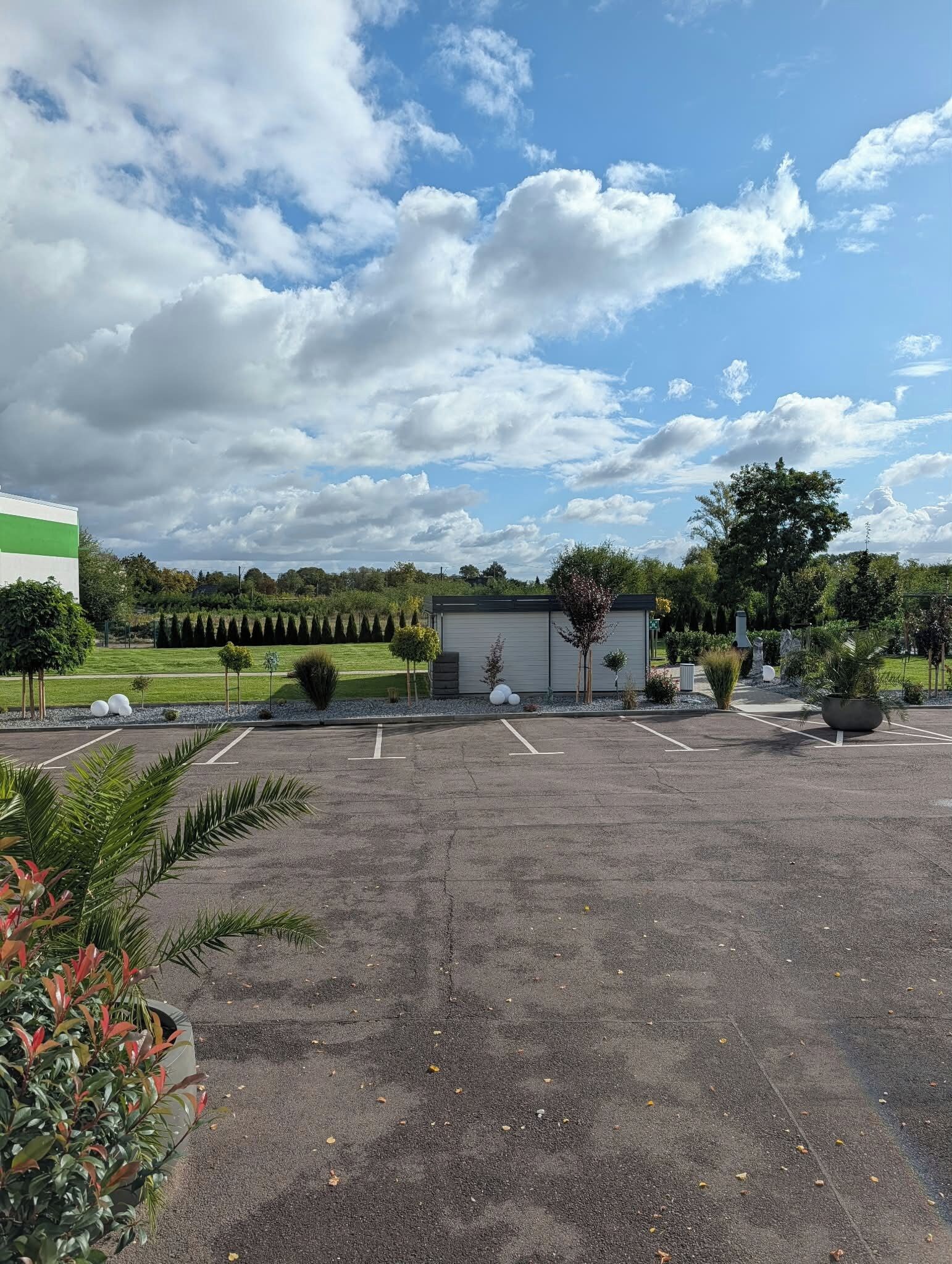Ein Parkplatz mit einem Gebäude, Bäumen und blauem Himmel.