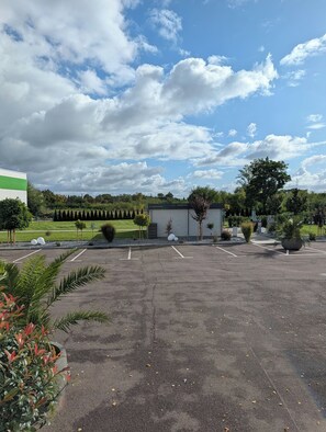Un parking avec un bâtiment, des arbres et un ciel dégagé.