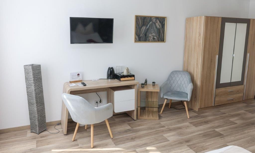 Une chambre moderne équipée d’un bureau, de deux chaises, d’une télévision, d’une armoire et d’une machine à café.
