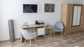 Une chambre moderne équipée d’un bureau, de deux chaises, d’une télévision, d’une armoire et d’une machine à café.