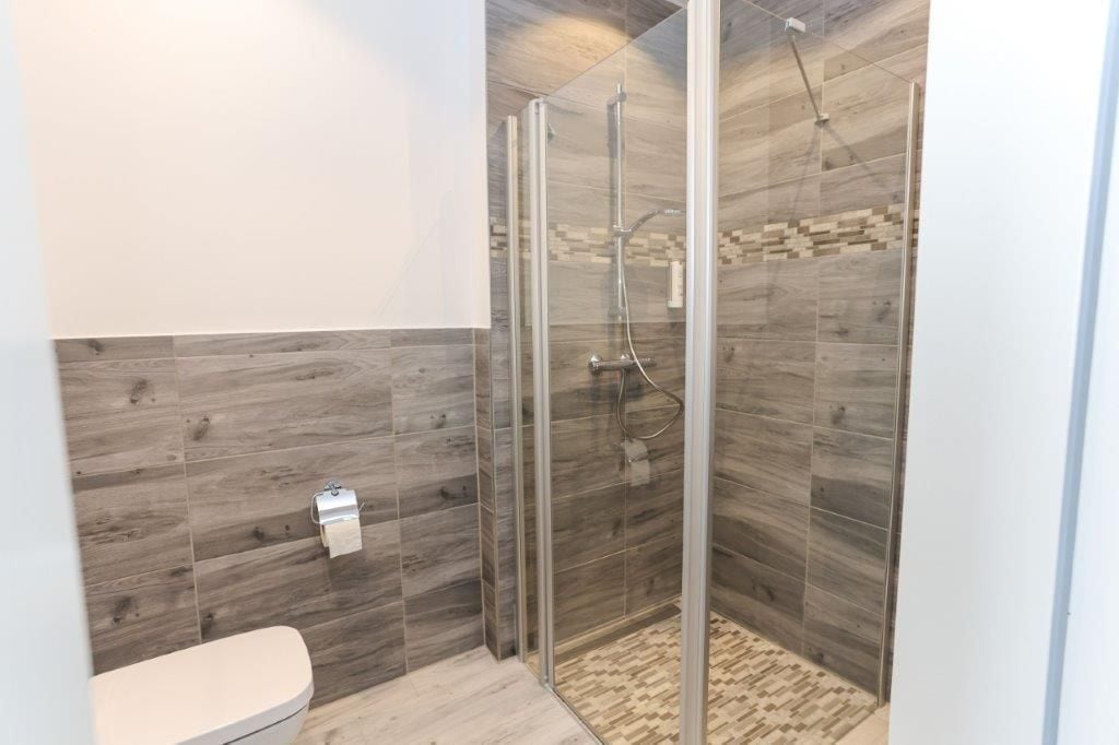 Un baño moderno con ducha acristalada, inodoro y suelo estampado.