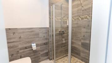 Un baño moderno con ducha acristalada, inodoro y suelo estampado.