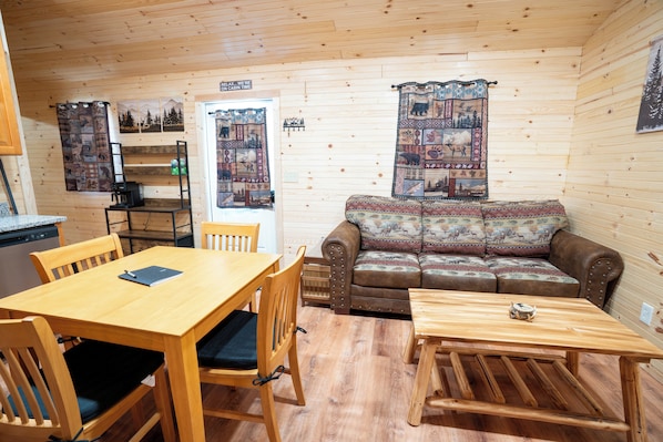 A cabin interior with a wooden dining table, chairs, a sofa, and a small wooden table.