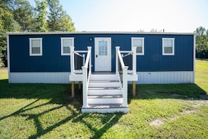 A single-story blue house with a white front door, two windows on the side, and a small porch with steps leading to the door. - Cozy 2-bedroom cabin with AC in Jacksonville, Alabama (Jacksonville)