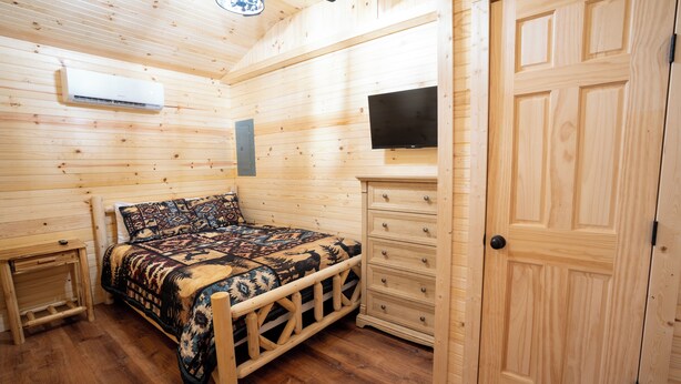 Een kamer met houten lambrisering, een bed, een dressoir, een televisie en een deur.