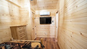 Een kleine kamer met houten wanden, een bed, een kapstok en een televisie aan de muur.