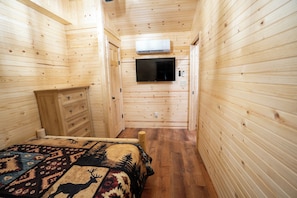A narrow wooden room with a bed, a dresser, and a television mounted on the wall. - Cozy 2-bedroom cabin with AC in Jacksonville, Alabama (Jacksonville)
