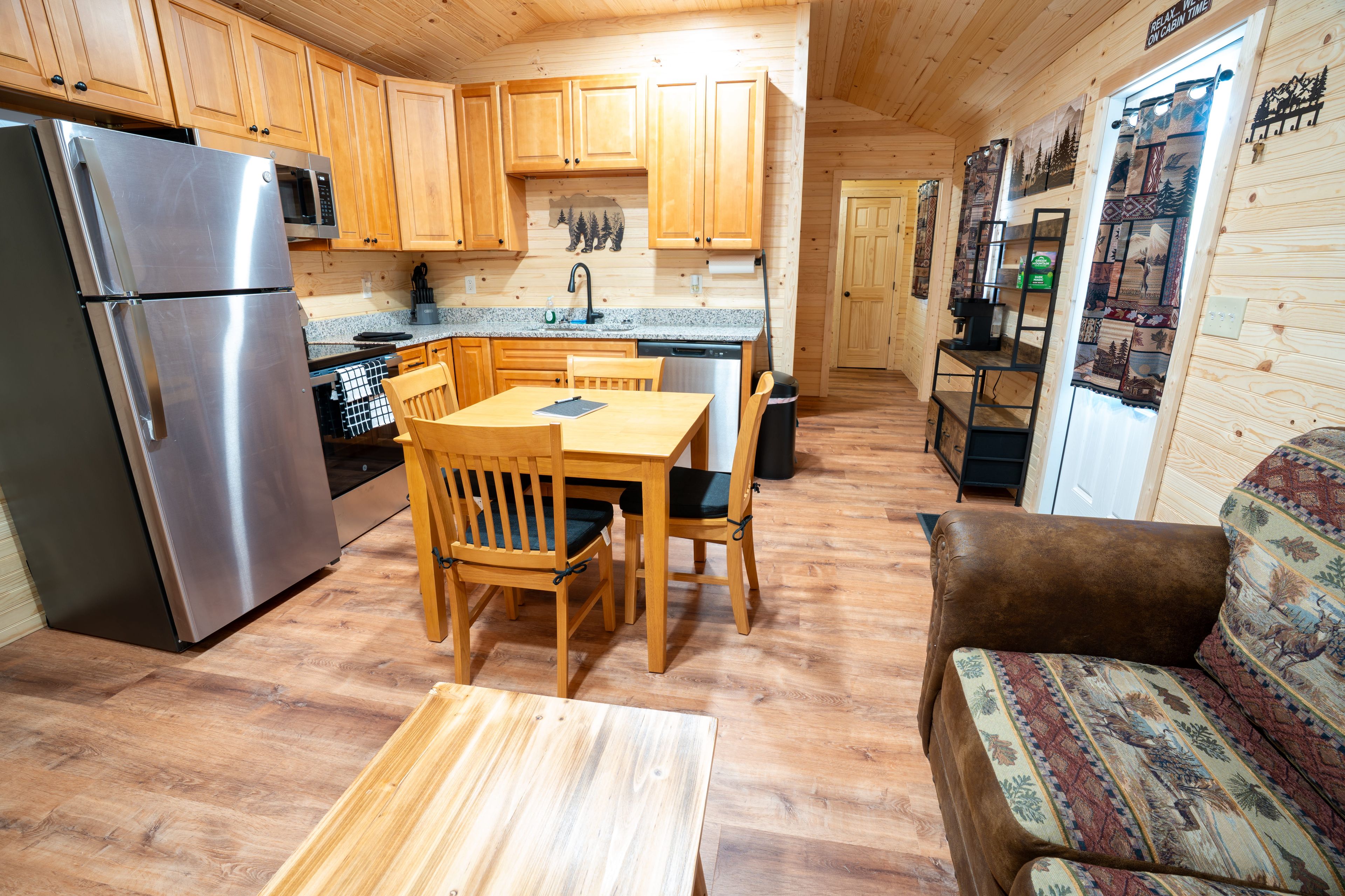 A compact kitchen with wooden cabinets, a stainless steel refrigerator, a microwave, and a coffee machine.