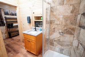 A bathroom with a shower, a sink, and wooden cabinetry. - Cozy 2-bedroom cabin with AC in Jacksonville, Alabama (Jacksonville)