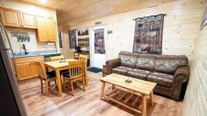 Een chaletinterieur met houten vloeren, een eettafel met stoelen, een bank en een keuken met kastjes en een koelkast.