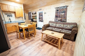 A cabin interior with wooden floors, a dining table with chairs, a sofa, and a kitchen area with cabinets and a refrigerator. - Cozy 2-bedroom cabin with AC in Jacksonville, Alabama (Jacksonville)