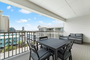 A balcony with a table and chairs, a grill, and a view of buildings. - Sea Glass 411 (Gulf Shores)