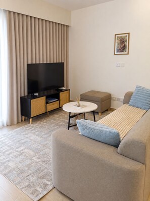 A modern living room with a sofa, a television, a small table, and a decorative item on the wall. - Modern 1BR SouthPark Near JKIA (Nairobi)