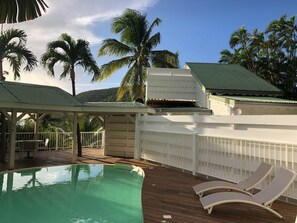 Ein Poolbereich mit Liegestühlen, einer überdachten Lounge und Palmen.