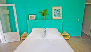 Ein Zimmer mit einem Bett, zwei Nachttischen, einer Tür und einer Wand mit zwei gerahmten Bildern.