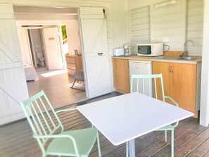 Eine kompakte Küche mit Mikrowelle, Spüle und kleinem Kühlschrank. Es gibt eine Essecke mit Tisch und Stühlen.