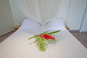 Ein Bett mit Baldachin, zwei Kissen, ein Nachttisch mit Lampe und eine Zierpflanze.