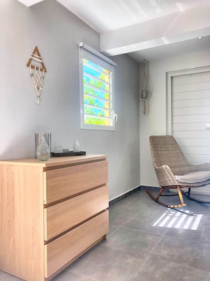 Ein Zimmer mit einem Holzkleiderschrank, einem Schaukelstuhl, einem Fenster mit Jalousien und einer Wandleuchte.