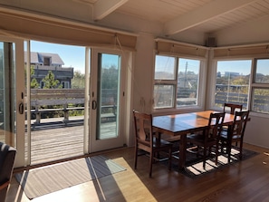 Ein Essbereich mit Holztisch und Stühlen, großen Fenstern und Blick auf eine Terrasse sowie Gebäude im Freien.