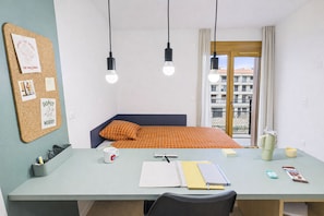 A room with a bed, a desk with a notebook, a mug, and a window with a view of buildings. - Kley Paris-Saint-Ouen (Saint-Ouen-sur-Seine)