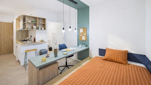 Une pièce de taille modeste comprenant un lit, un bureau et une kitchenette.