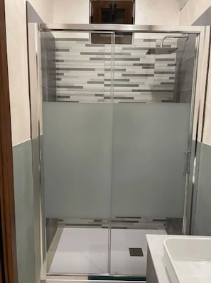 Ein modernes Badezimmer mit einer begehbaren Glasdusche, einem weißen Waschbecken und einer gefliesten Spritzschutzwand.