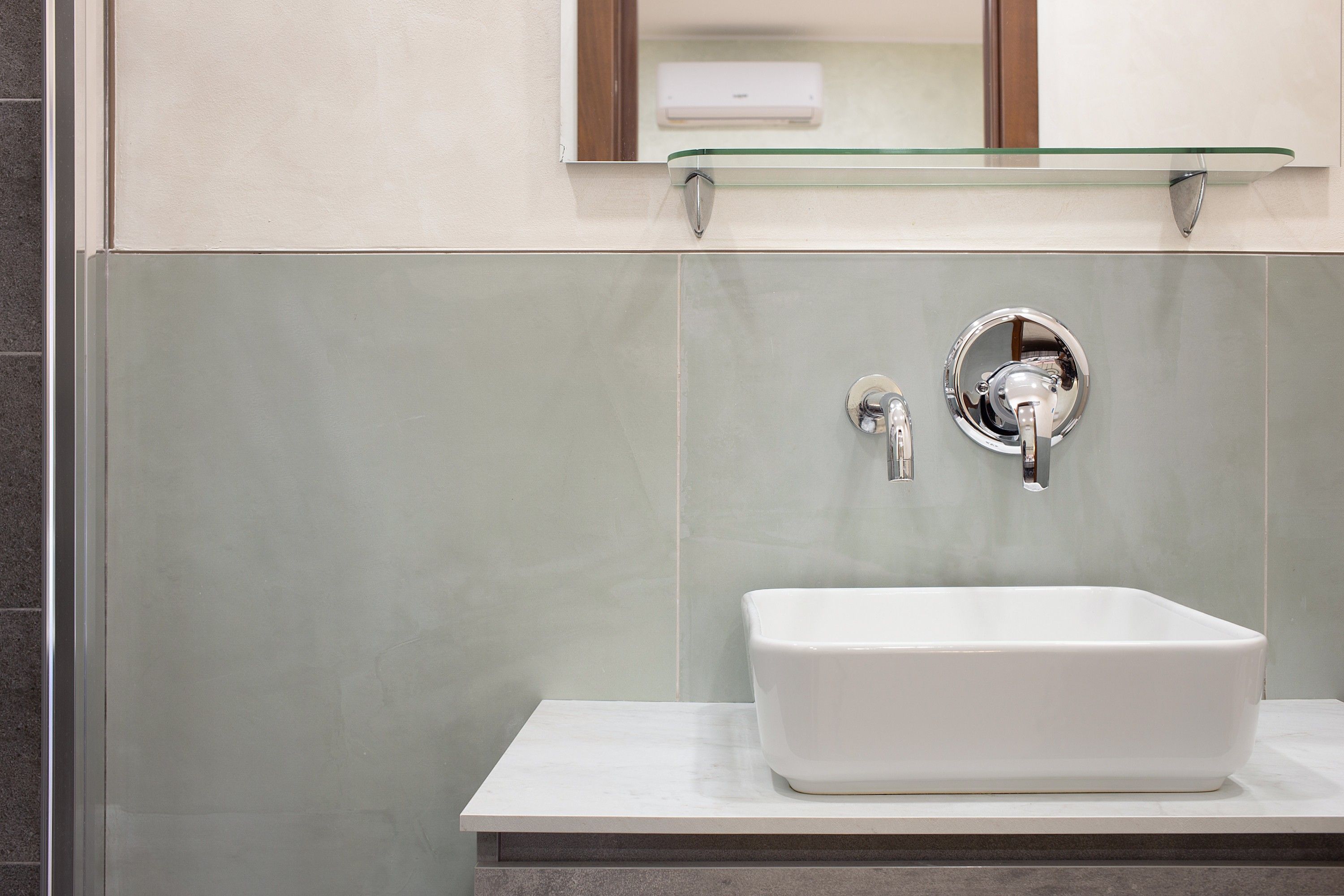 Un bagno con un lavandino bianco, uno scaffale in vetro sopra il lavandino e uno specchio con cornice in legno.