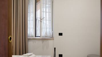 Una habitación con una cama, una ventana con cortinas, una puerta y un taburete pequeño.