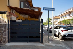 A gated entrance to a property with a blue directional sign, a stone wall, and parked cars.