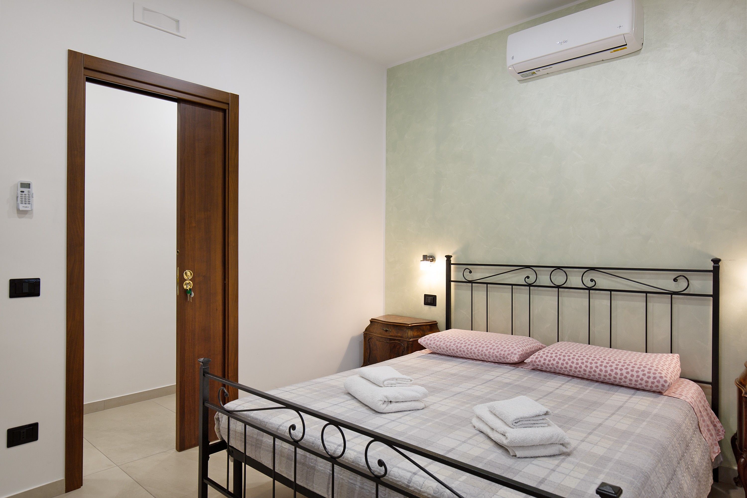 Una camera da letto con un letto, un comodino, un condizionatore d'aria a parete e una porta.