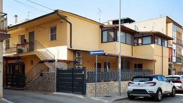 A yellow building with a black gate, a staircase, and a parked white car.
