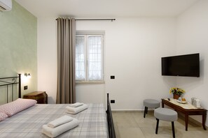 A bedroom with a bed, a desk, a television, and a window with curtains.