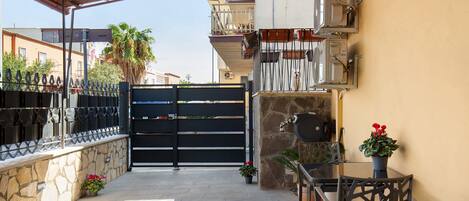 An outdoor patio area with a stone wall, a metal gate, a table with chairs, and potted plants.
