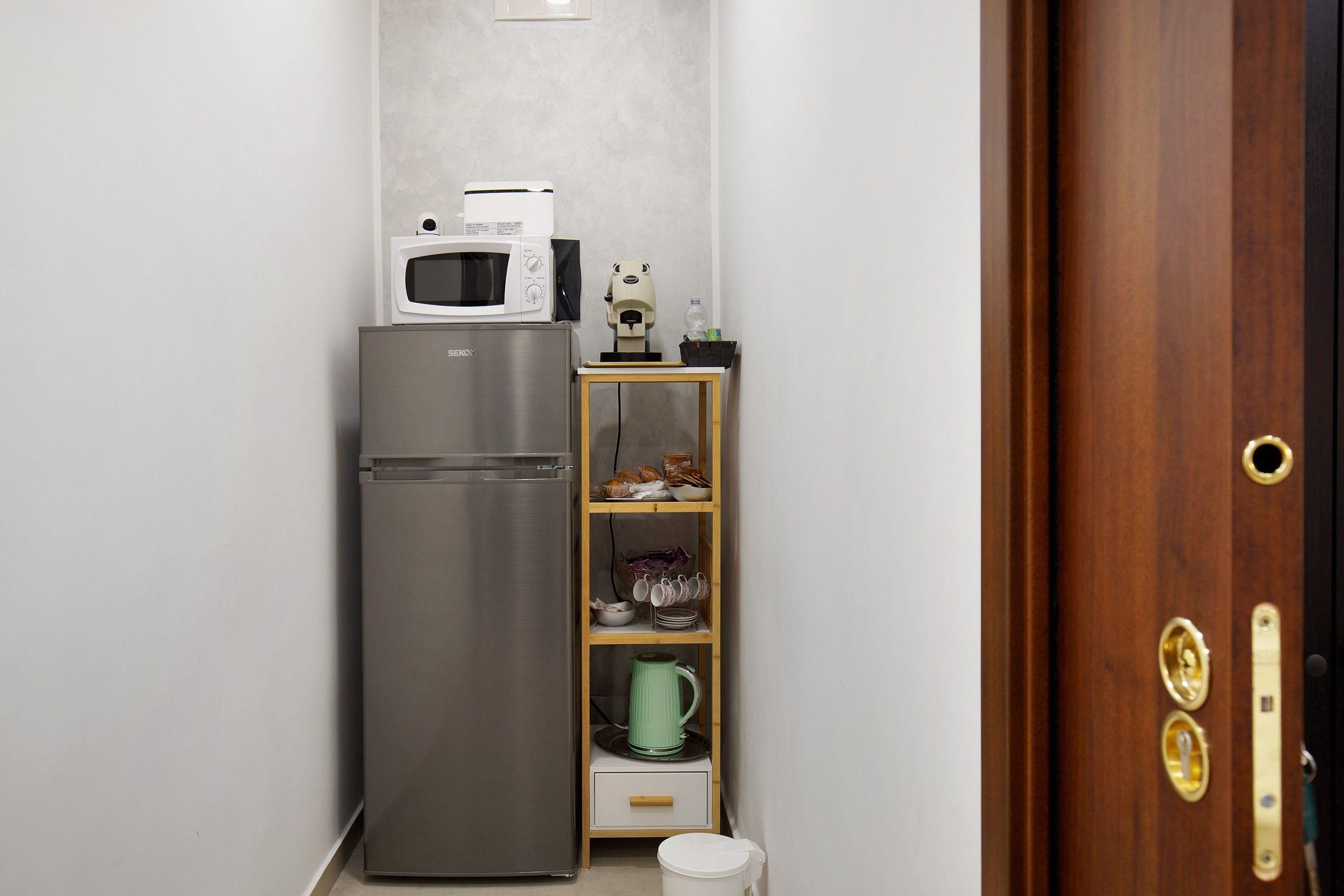 A compact kitchenette with a refrigerator, microwave, and a small cabinet with dishes.