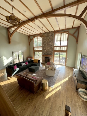 A spacious living room with a stone fireplace, large windows, and a wooden ceiling structure. - Pen y Bryn - 5BR Blue Ridge Luxury Retreat with Pool, Library & Game Room (Faber)