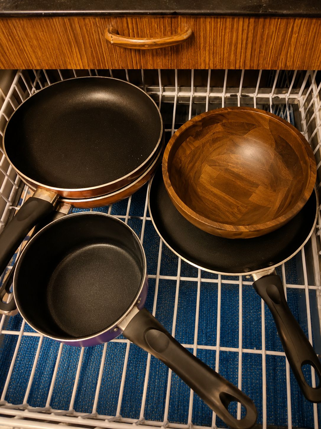 Un cajón de cocina con tres utensilios: dos sartenes y un bol de madera.