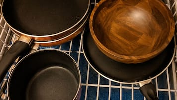 Un cajón de cocina con tres utensilios: dos sartenes y un bol de madera.