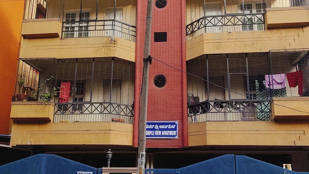A multi-story building with balconies, a central red pillar, and a blue gate in the foreground. - 2bhk Malleswaram templeview-veg only (Bengaluru)