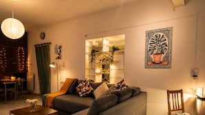 A modern living room with a sectional sofa, a coffee table, a patterned rug, a wooden chair, a decorative wall piece, and a ceiling fan. - 2bhk Malleswaram templeview-veg only (Bengaluru)