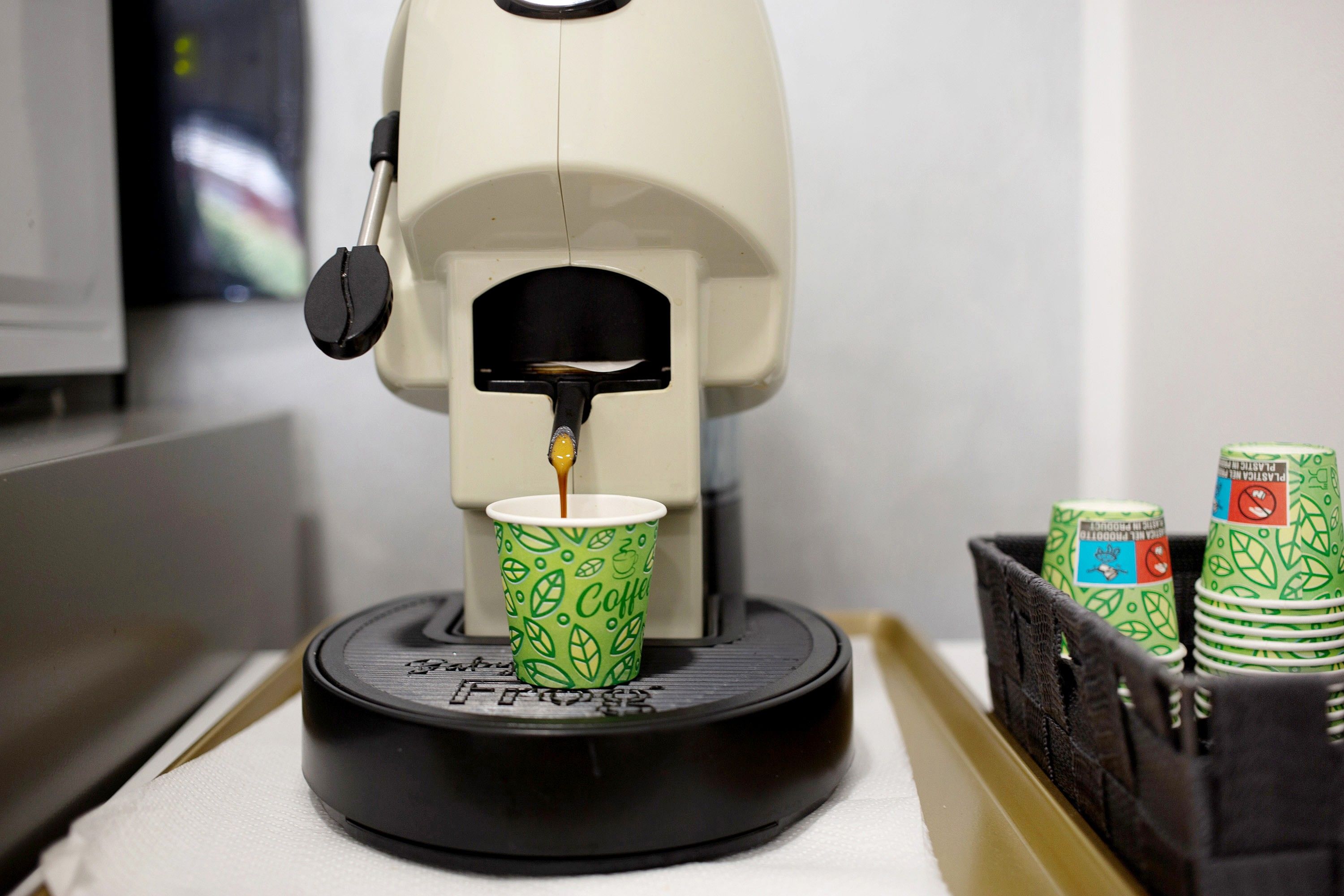 A coffee machine dispensing coffee into a paper cup with a leaf pattern.