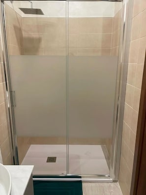 Une cabine de douche fermée par des parois en verre, dotée d’un sol carrelé et d’un drain visible.